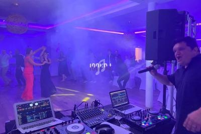 Des personnes dansent sur une piste éclairée de lumières colorées, avec un DJ et un animateur au premier plan.