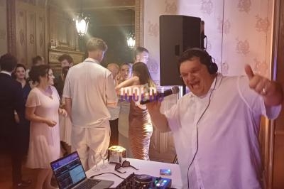 Un DJ souriant anime une soirée dansante dans une salle élégante avec des invités en arrière-plan.