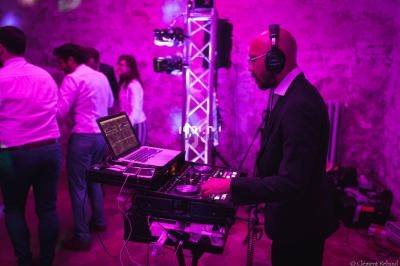 Un DJ en costume mixe de la musique sur une console lors d'une soirée dans une ambiance lumineuse violette.