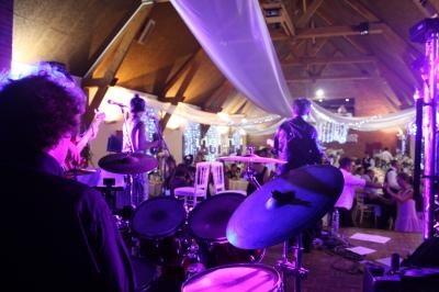 Musiciens jouant sur scène dans une salle décorée de guirlandes lumineuses, avec un public en arrière-plan.