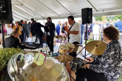 Musiciens jouant en groupe sous une tente lors d'un événement en plein air avec des invités en arrière-plan.