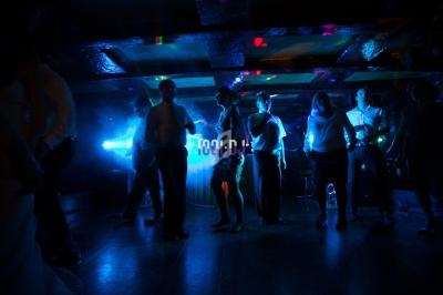 Des personnes dansent dans une salle sombre éclairée par des lumières colorées et un projecteur lumineux.