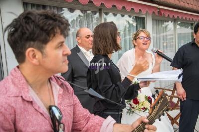 Un groupe de personnes chante et joue de la musique lors d'un événement en extérieur, avec une mariée au micro.