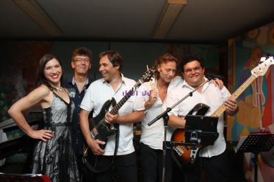 Un groupe de musiciens souriants posant avec leurs instruments dans une salle décorée.