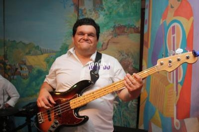 Un musicien souriant joue de la guitare basse dans un décor coloré avec des peintures murales.