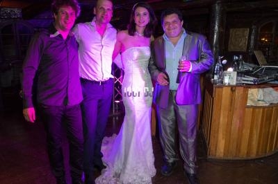 Quatre personnes posent souriantes dans un lieu éclairé par des lumières colorées, dont une femme en robe de mariée.