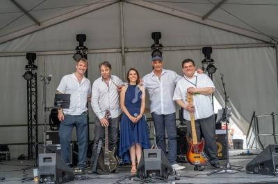 Un groupe de cinq musiciens pose sur une scène sous une tente, entouré d'instruments et d'équipements.