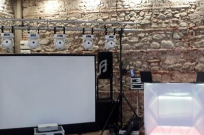 Installation d'équipements audiovisuels avec projecteurs suspendus, écran blanc et mur en pierre en arrière-plan.
