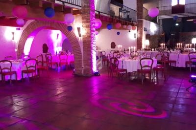 Salle de réception décorée avec des tables rondes, des chaises en bois et des éclairages violets.
