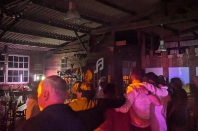 Groupe de personnes dansant dans une salle faiblement éclairée avec des lumières colorées et un DJ en arrière-plan.
