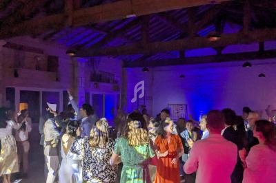 Des personnes dansent dans une salle éclairée par des lumières colorées, avec un plafond en bois visible.