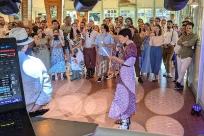 Une femme lit un discours devant un groupe de personnes rassemblées dans une salle lumineuse lors d'un événement festif.