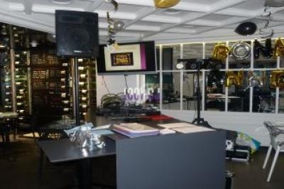 Salle décorée pour une fête, avec une table, des ballons ’Bonne Année’, des équipements audio et un éclairage festif.