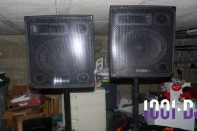 Deux enceintes noires sur pied dans un sous-sol encombré.