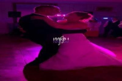 Un couple danse sous une lumière rose dans une salle sombre, entouré de quelques invités en arrière-plan.