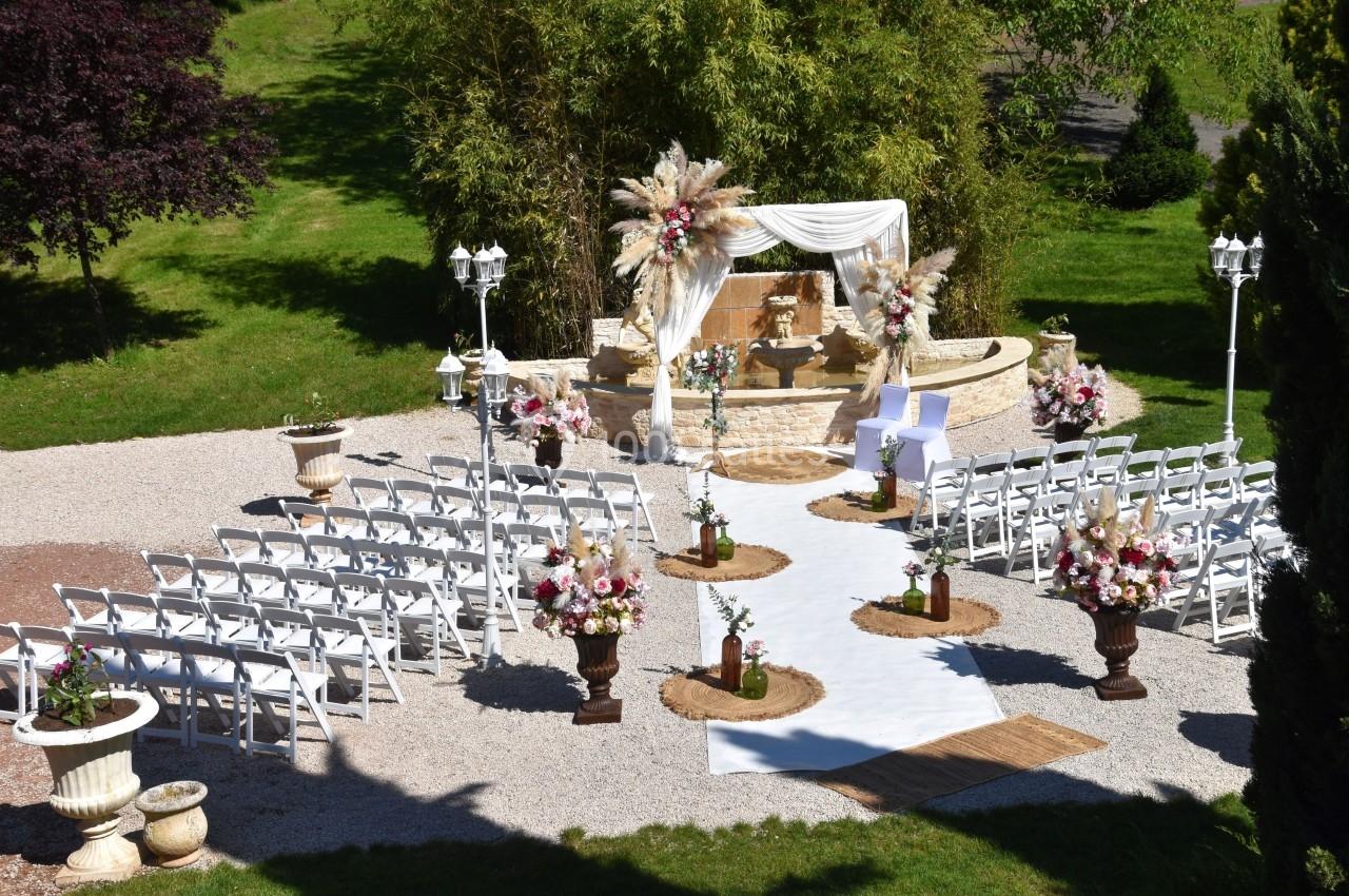 Cérémonie de mariage en extérieur avec une arche décorée de fleurs, des chaises blanches et une allée centrale.