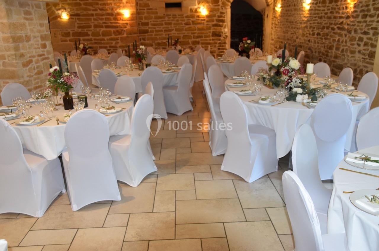 Salle de réception en pierre avec tables rondes dressées, nappes blanches et décorations florales.