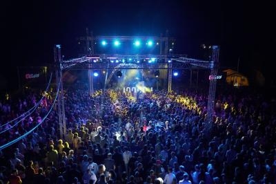 Foule rassemblée devant une scène illuminée par des projecteurs colorés lors d'un concert en plein air de nuit.