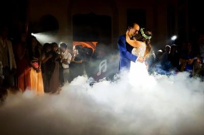 Un couple danse au milieu d'une piste entourée de fumée, sous un éclairage tamisé, devant des invités.