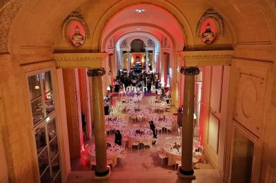 Salle de réception élégante avec tables rondes dressées, éclairage chaleureux et architecture classique.