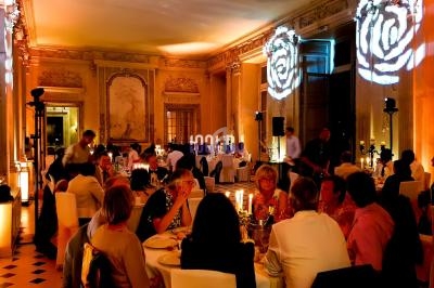 Salle élégante avec invités dînant à des tables éclairées par des bougies, décorations lumineuses projetées sur les murs.