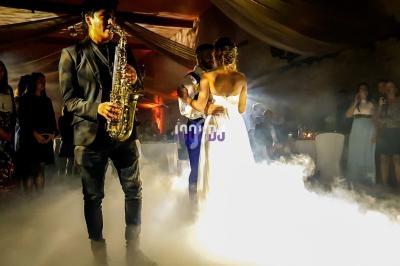 Un couple danse dans une salle éclairée, entouré de fumée, tandis qu'un musicien joue du saxophone au premier plan.