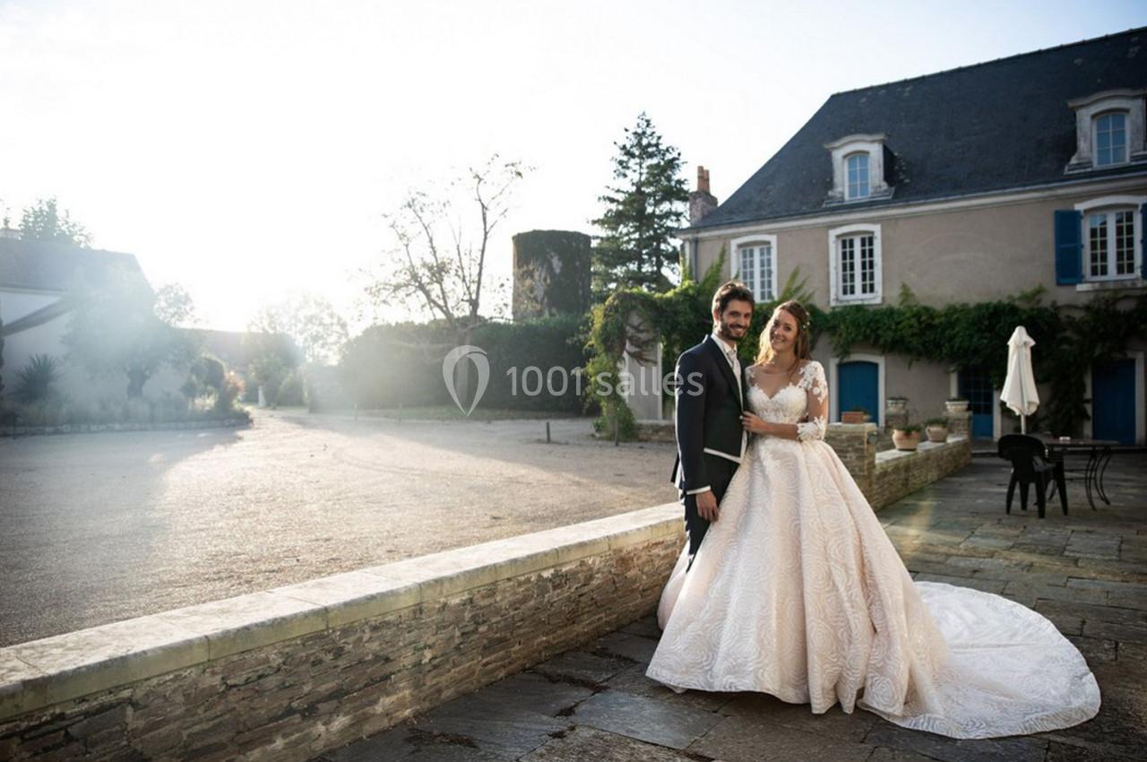 Un couple en tenue de mariage pose devant un bâtiment ancien avec des volets bleus, sous une lumière douce.