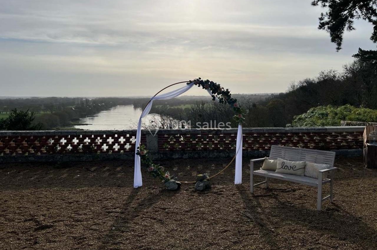 Arche décorée de fleurs et banc en bois avec coussin ’love’, surplombant une rivière et un paysage naturel.