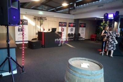 Salle de réception avec une table de mixage, des affiches promotionnelles et des invités debout près d'un tonneau.