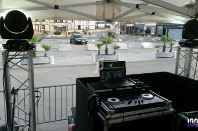 Équipement de DJ installé sous une tente, avec platines, enceintes et vue sur une place urbaine en arrière-plan.