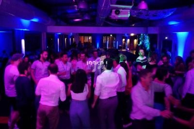 Groupe de personnes dansant dans une salle éclairée par des lumières colorées, vue depuis une table de mixage.