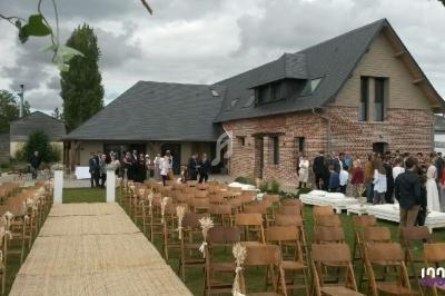 Chaises alignées et allée centrale en extérieur devant une maison en briques, avec des invités rassemblés au loin.
