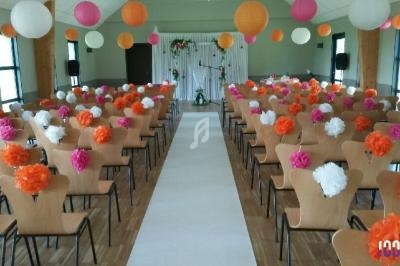 Salle décorée pour une cérémonie avec des chaises alignées, des lanternes et des pompons colorés suspendus.