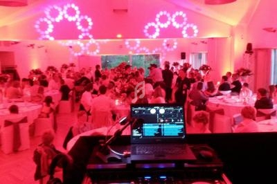 Salle de réception illuminée en rouge avec des invités assis à des tables et un poste de DJ au premier plan.