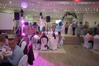Salle de réception décorée avec des guirlandes lumineuses, des invités assis à des tables rondes et une arche fleurie.