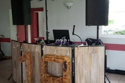 Console de DJ en bois avec éclairage, enceintes et décoration en forme de chiffre 18 dans une salle lumineuse.