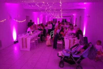 Salle de réception éclairée en rose avec des invités assis à des tables décorées, et des enfants au premier plan.