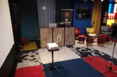 Salle équipée pour des présentations ou événements, avec un pupitre, un projecteur et des sièges colorés.