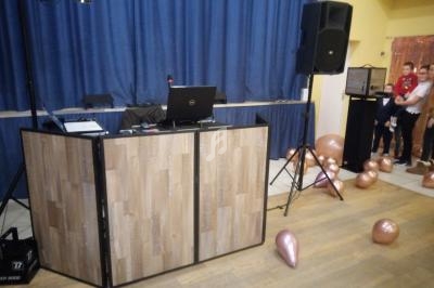 Poste de DJ avec ordinateur portable, enceintes et ballons dorés au sol dans une salle avec rideaux bleus.
