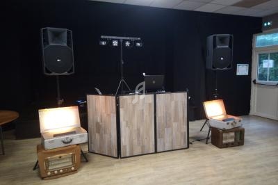 Installation de DJ avec une table en bois, deux enceintes, des lumières et des valises rétro éclairées dans une salle.