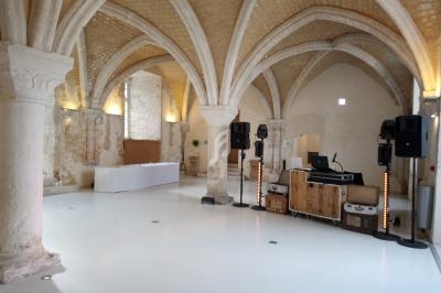 Salle voûtée en pierre avec un sol blanc, équipée de matériel de sonorisation et d'un espace pour DJ.