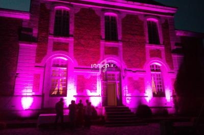 Façade d'un bâtiment en briques éclairée par des lumières roses, avec des silhouettes de personnes au premier plan.