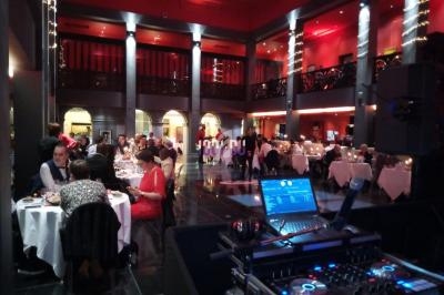 Salle de réception avec invités dînant à des tables rondes, éclairage tamisé et équipement de DJ au premier plan.