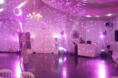 Salle de réception décorée avec des lumières violettes et un DJ installé derrière une table de mixage.