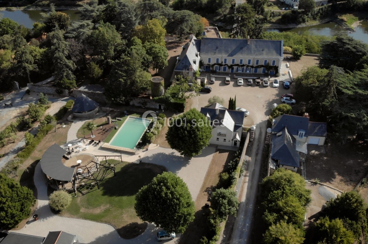 Vue aérienne d'un domaine avec bâtiments anciens, piscine, espaces verts et un parking, entouré de végétation.