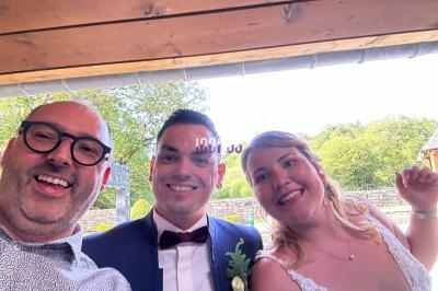 Trois personnes souriantes posent pour une photo sous un abri en bois, avec un paysage verdoyant en arrière-plan.