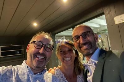 Trois personnes souriantes posent pour une photo dans un environnement intérieur sombre.
