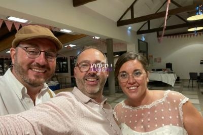 Trois personnes souriantes posent dans une salle décorée avec des guirlandes et des tables en arrière-plan.