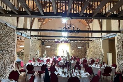 Salle de réception avec murs en pierre, poutres apparentes, tables rondes dressées et chaises rouges.