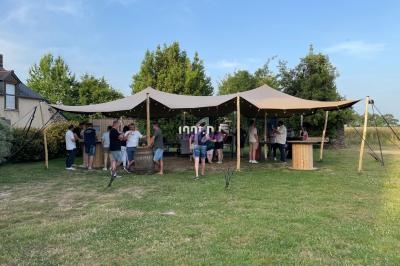 Groupe de personnes rassemblées sous une grande tente beige dans un jardin par temps ensoleillé.